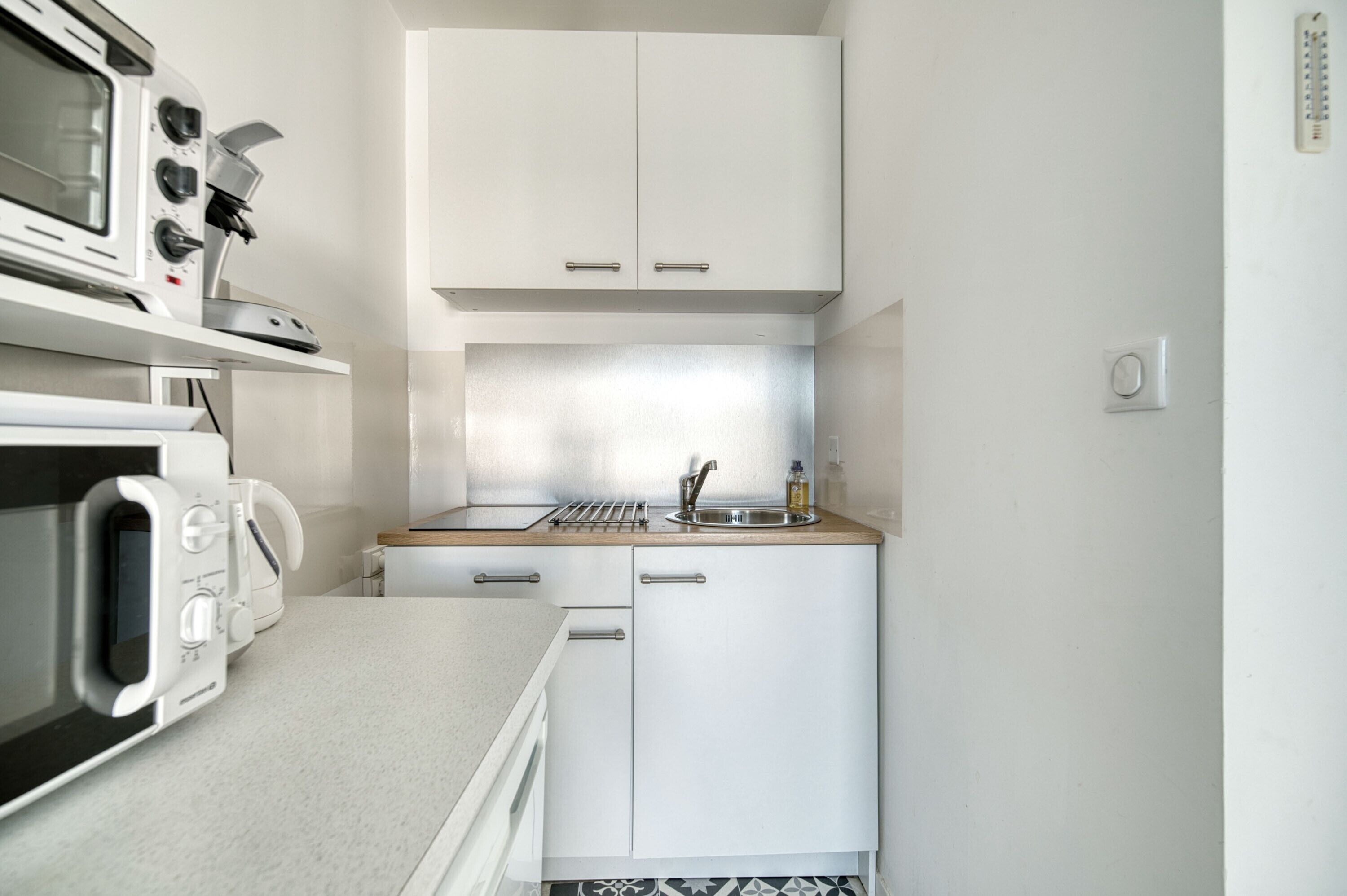 Una cucina compatta con mobili bianchi, un forno a microonde, un fornello e un lavandino.