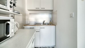 A compact kitchen with white cabinets, a microwave, a stove, and a sink.