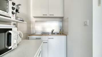 Una cucina compatta con mobili bianchi, un forno a microonde, un fornello e un lavandino.