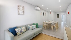 A modern living room with a grey sofa, a dining area with wooden chairs, and a kitchen area. - Apartment 'Eanes 22 Beach House' with Balcony, Wi-Fi and Air Conditioning (Monte Gordo)