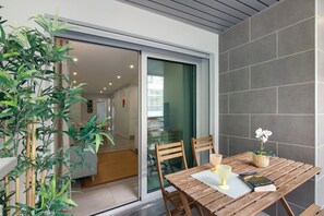 A wooden table with chairs, a glass, a book, and a potted plant in a modern room with a sliding glass door.