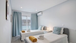 A hotel room with two beds, a window with curtains, an air conditioning unit, and a view of the outside. - Apartment 'Eanes 22 Beach House' with Balcony, Wi-Fi and Air Conditioning (Monte Gordo)