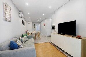 A modern living room with a flat-screen TV, a sofa, and a dining area in the background.