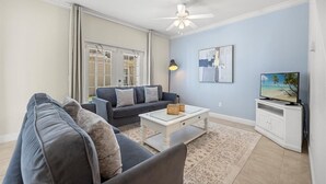 Un salon avec un canapé, une table basse, un téléviseur et des œuvres d’art accrochées au mur.