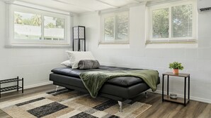 Un dormitorio moderno con un sofá de cuero negro, una alfombra estampada y una mesita de noche con una planta.