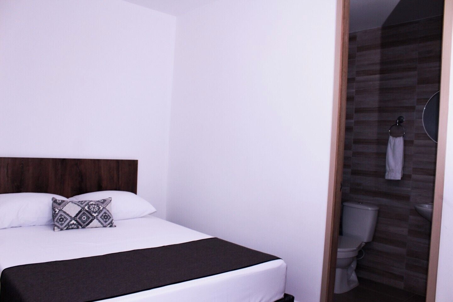 A modern hotel room with a large bed, a wooden headboard, a patterned pillow, and a black throw blanket.