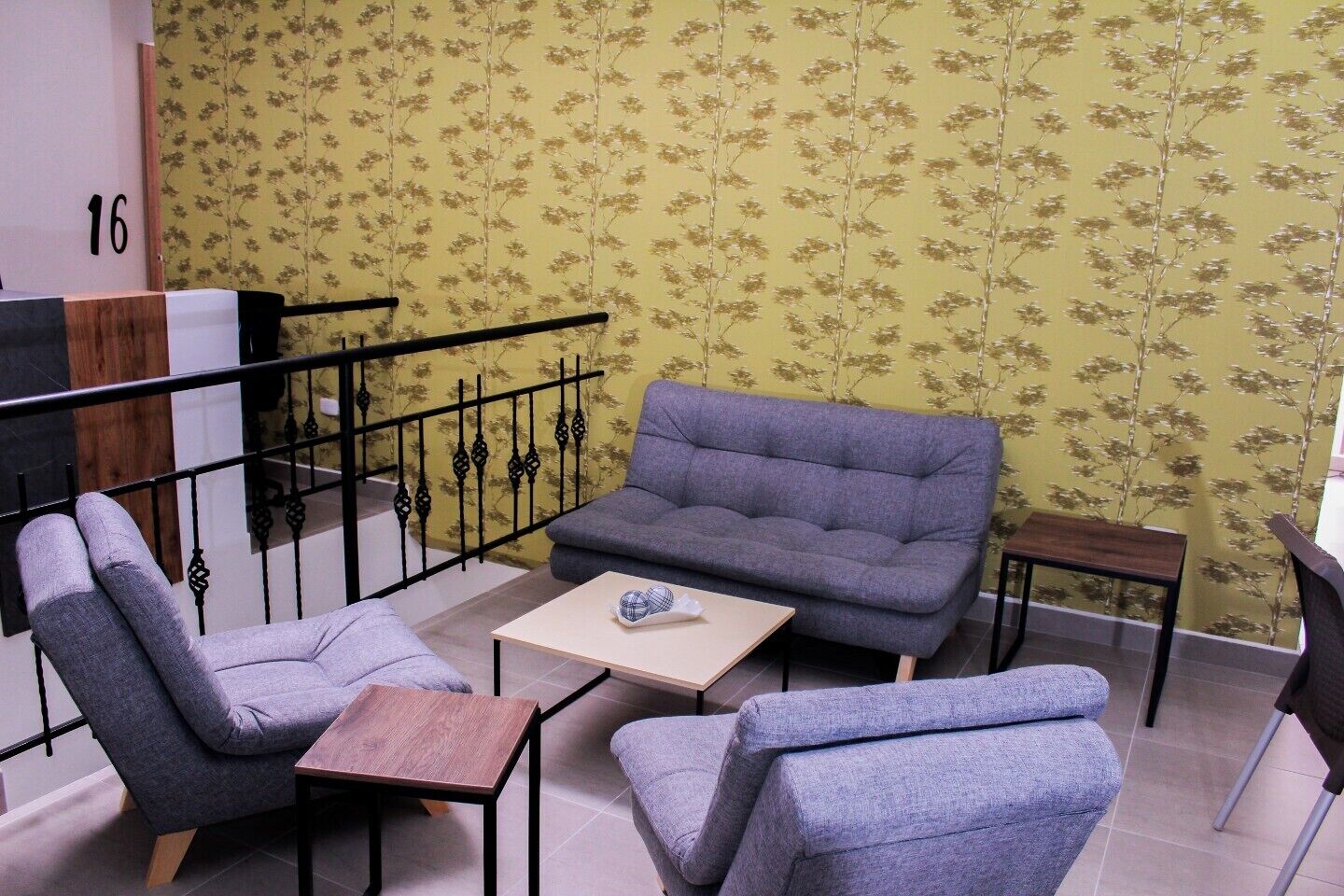 A living room with a grey sofa, two armchairs, a small wooden table, and a patterned wallpaper.