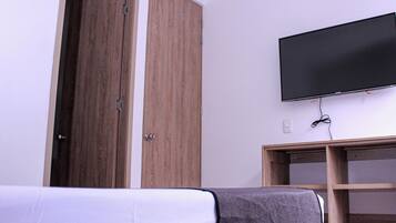 A bedroom with a bed, a wardrobe, a television mounted on the wall, and a wooden cabinet.