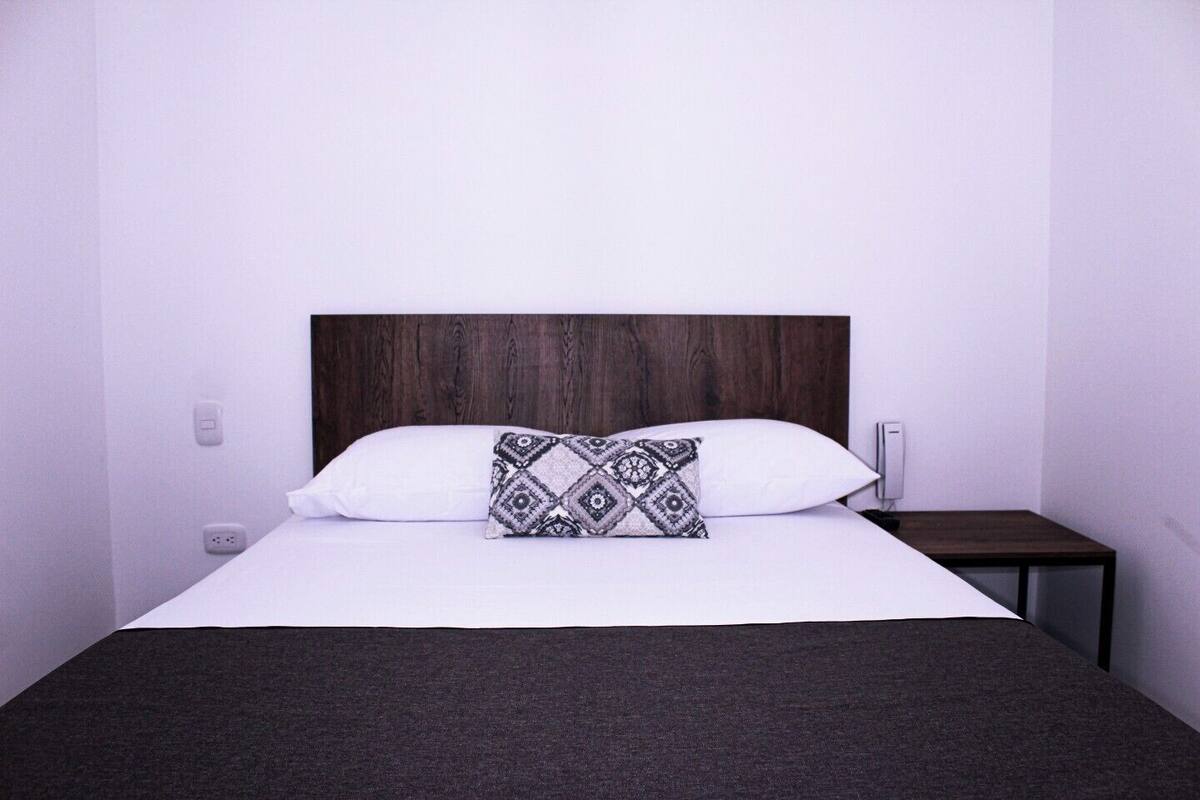 Un lit avec une tête de lit sombre, une literie blanche et un coussin à motifs.