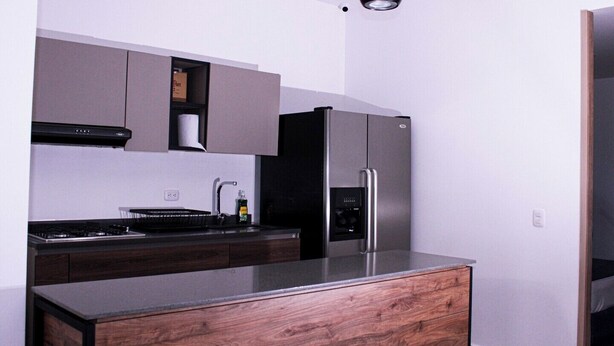 A modern kitchen with a built-in stove, stainless steel refrigerator, and wooden cabinetry. - Ayenda Hotel MM (Pereira)