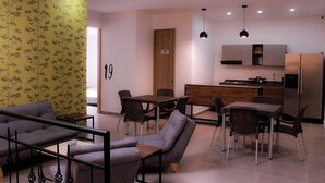A modern living room with a sofa, chairs, and a dining table. There is a kitchen area with a refrigerator and cabinets. - Ayenda Hotel MM (Pereira)