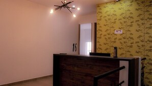 A reception desk with a wooden finish, a modern light fixture, and a floral wallpaper pattern on the adjacent wall. - Ayenda Hotel MM (Pereira)
