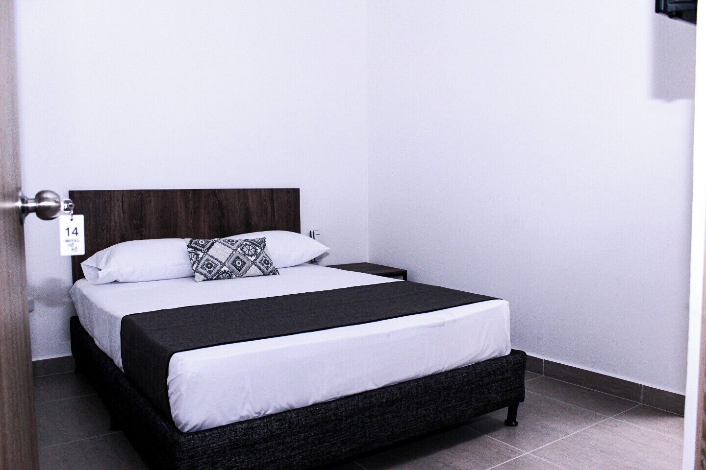 Un lit simple avec une tête de lit sombre, une literie blanche et un coussin à motifs.