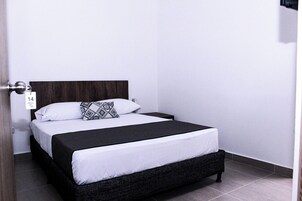 Una cama individual con cabecera oscura, ropa de cama blanca y almohada estampada.
