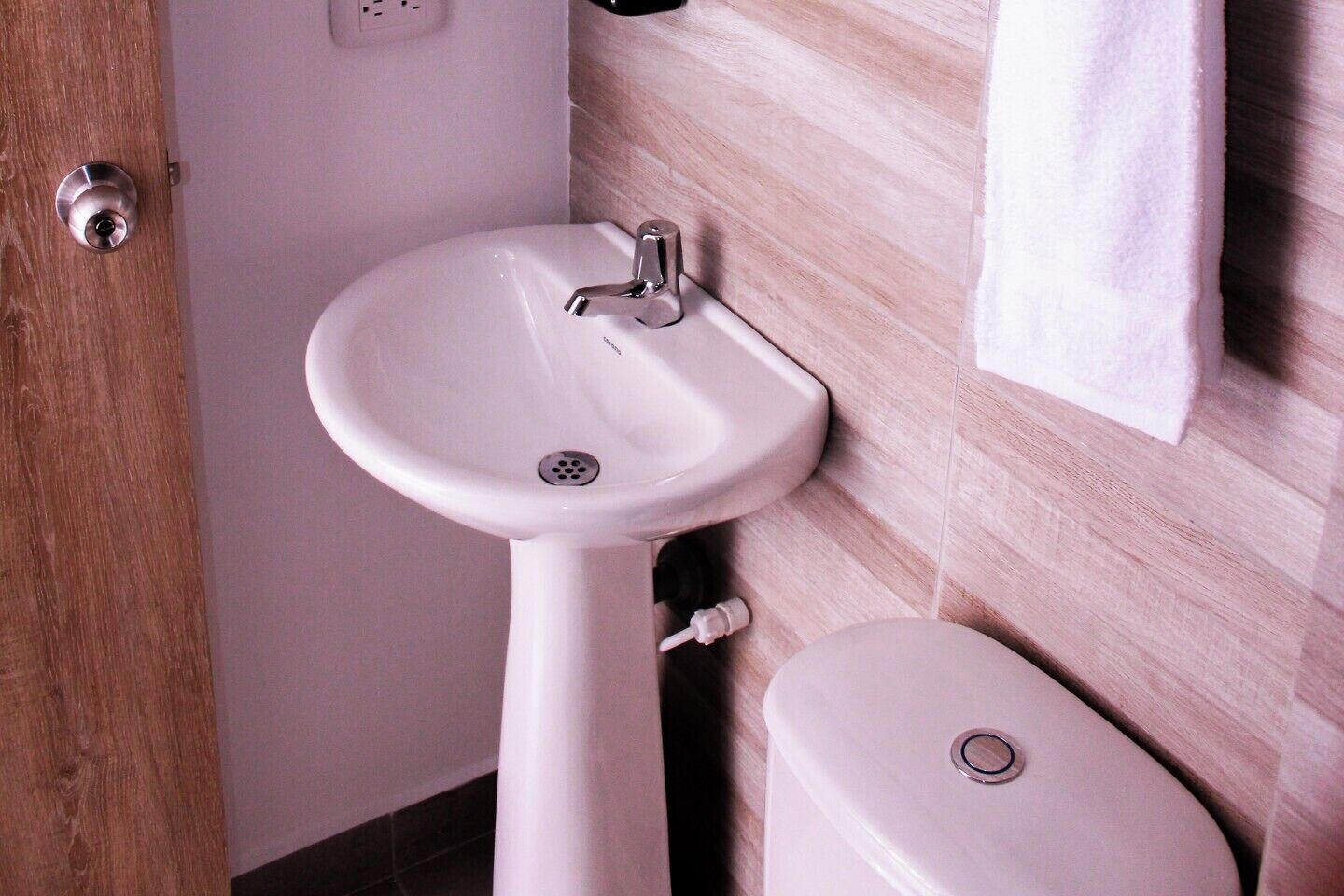 A bathroom with a white pedestal sink, a toilet, and a wooden door.