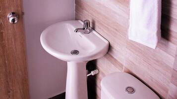 A bathroom with a white pedestal sink, a toilet, and a wooden door.