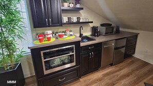 A compact kitchen with dark cabinets, a microwave, a coffee maker, and a sink. There is a shelf above the sink with decorative items and a potted plant. - Beautiful LOFT SUITE, Private Guest House located in Hamlet of Mirror. (Mirror)