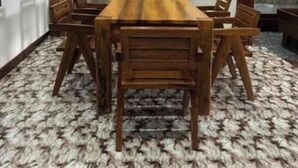 Une salle de conférence avec une table et des chaises en bois, une petite table d’appoint avec une lampe et un tapis à motifs.