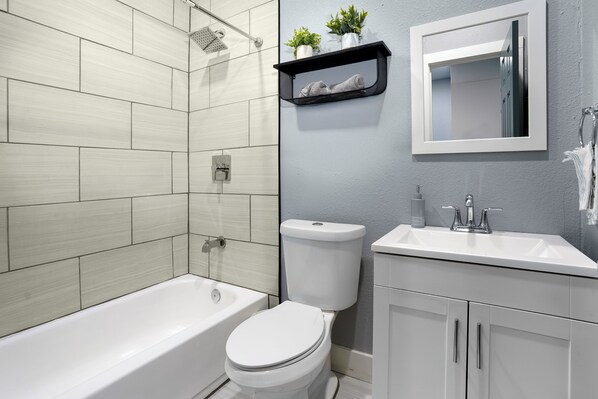 Une salle de bain moderne avec une baignoire blanche, des toilettes et un lavabo surmonté d’un miroir.
