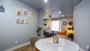 Ein modernes Wohnzimmer mit einem runden Marmortisch, einem Deckenventilator und einer Couch mit Kissen.