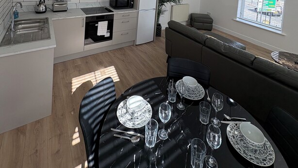 A modern kitchen with white cabinets, a dining area with a black table set for six, and a large window with a view of the street. - 2 x bed city apartment with parking  (Hull)