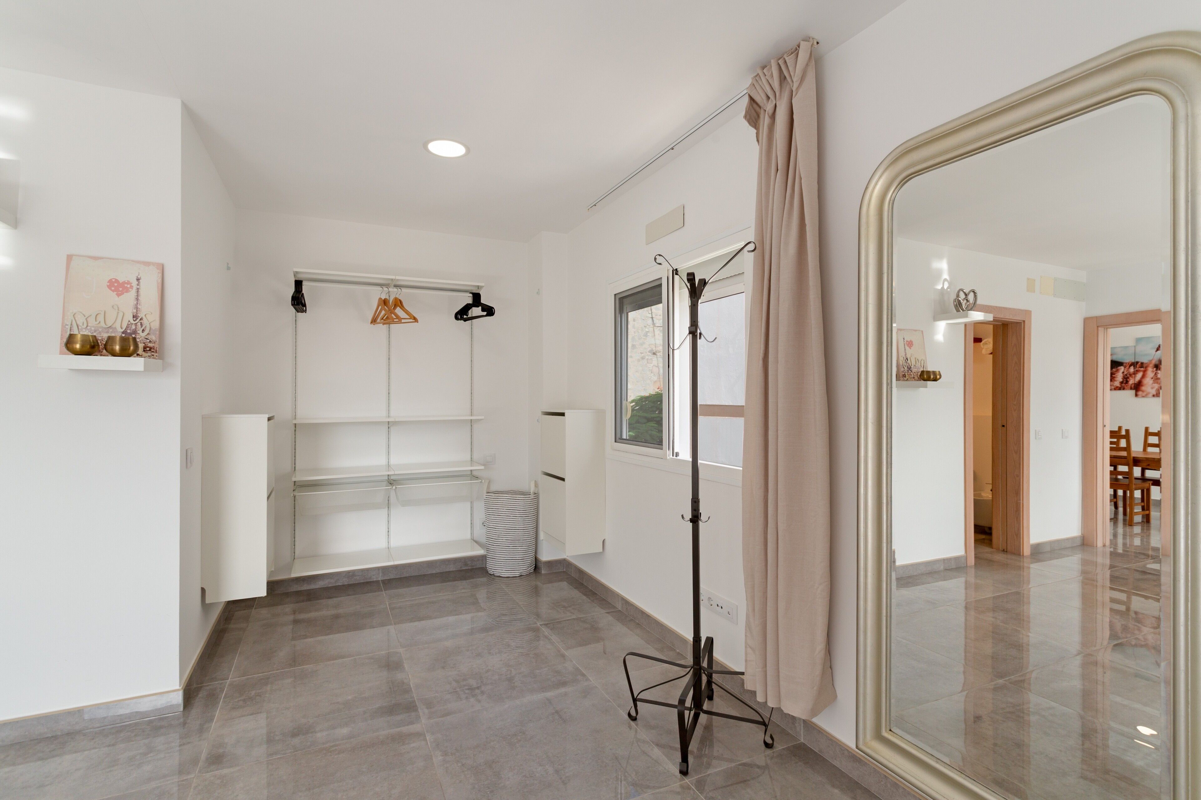 Una habitación de hotel con un espejo grande, un armario, un perchero y una ventana con cortinas.