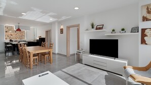 Una sala de estar moderna con comedor, televisor y cocina al fondo.