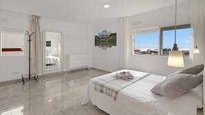 Un dormitorio moderno con cama, vistas a la ciudad, un perchero y un cuadro en la pared.