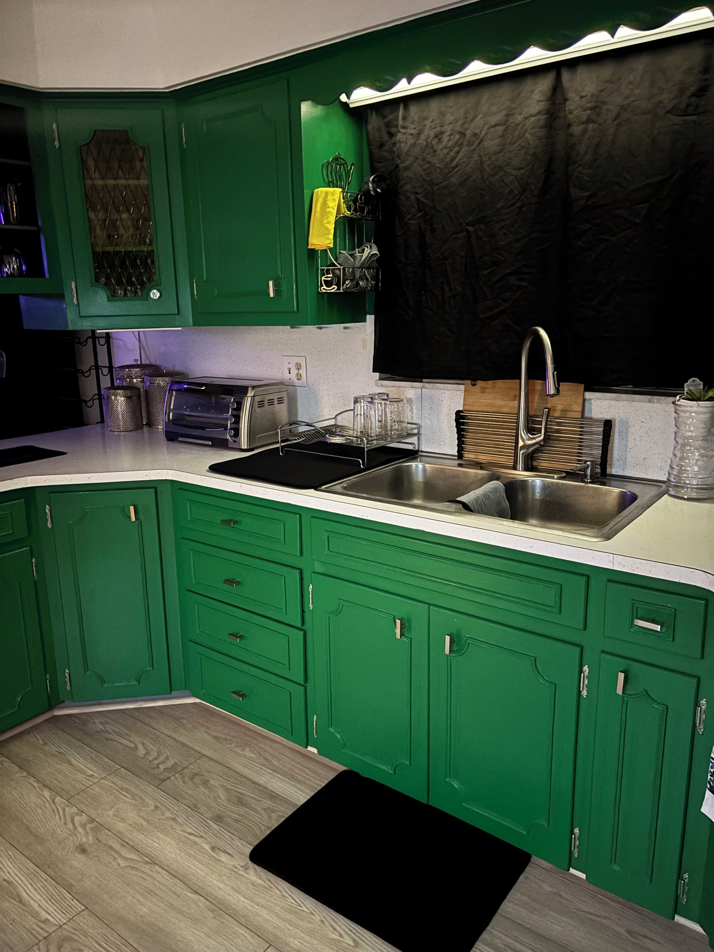A kitchen with green cabinets, a black countertop, a stainless steel sink, and a toaster.