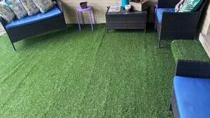 A patio area with artificial grass, wicker furniture, and decorative pillows. - Sunburst Palace Spacious 4-bedrooms a Den-Fulton with AC in Center Line, MI. (Center Line)