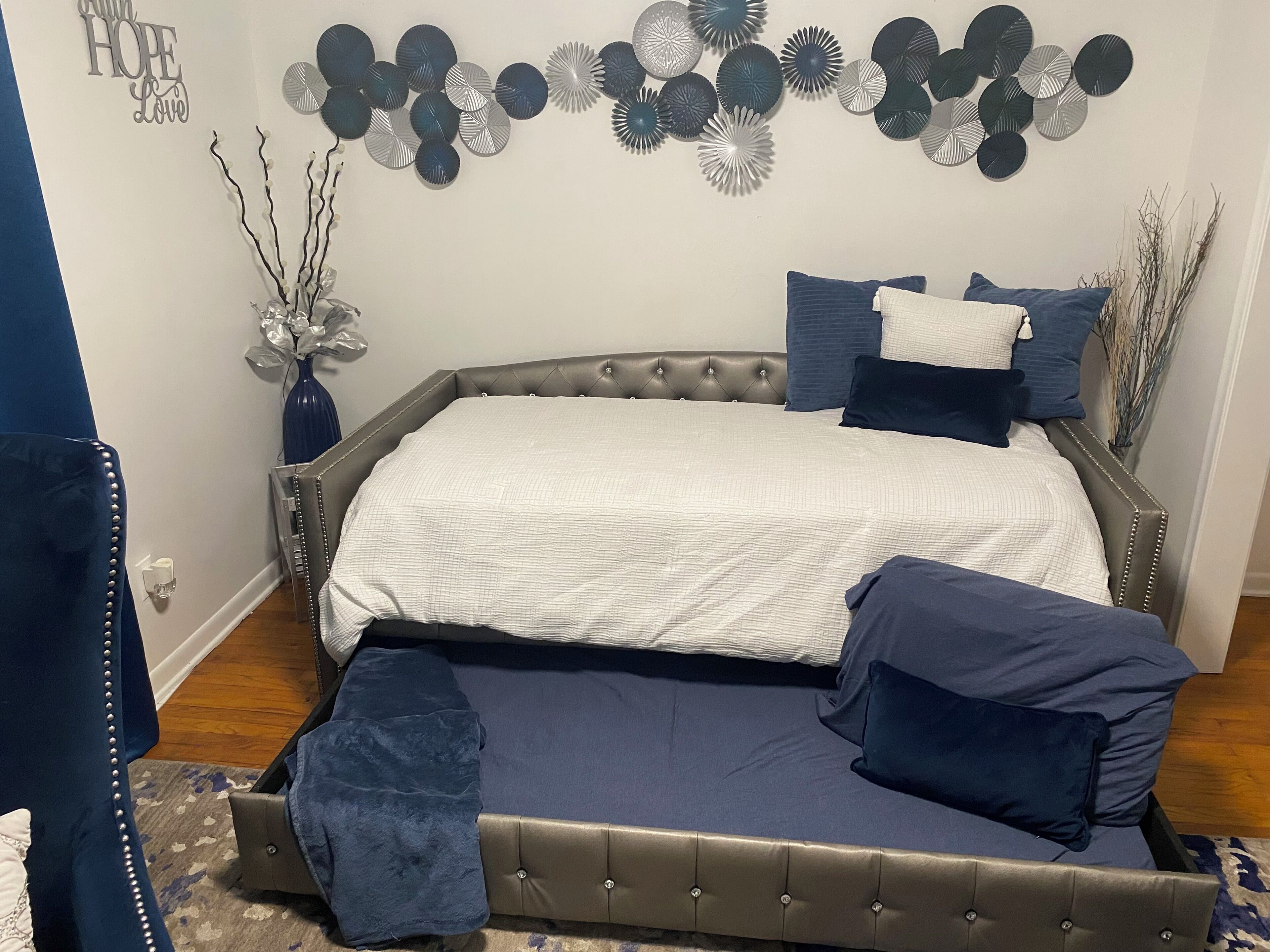Une chambre à coucher avec une tête de lit capitonnée, un lit recouvert d’une courtepointe blanche et une literie bleu foncé.