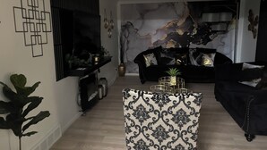 A modern living room with a black sofa, a patterned ottoman, and a marble wall. - Sunburst Palace Spacious 4-bedrooms a Den-Fulton with AC in Center Line, MI. (Center Line)