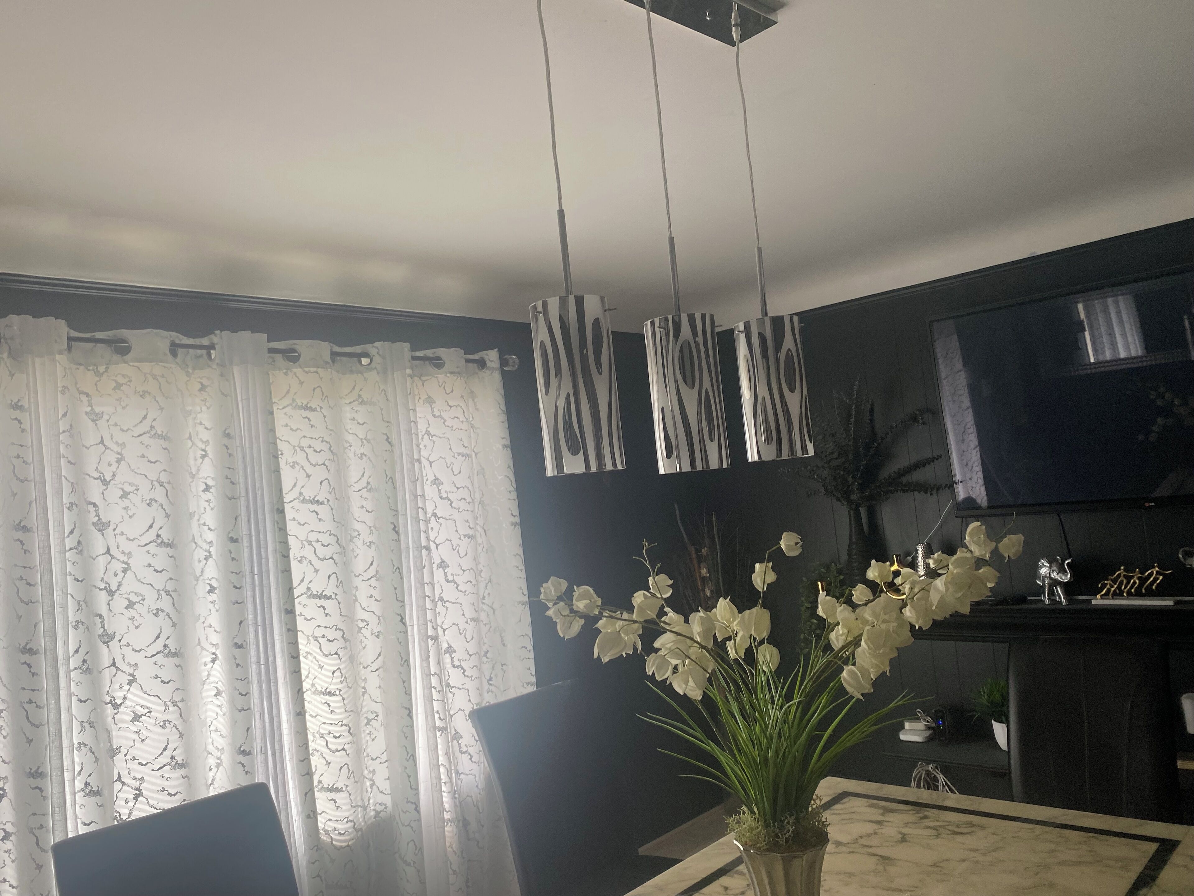 A living room with a TV, a vase with flowers, and a curtain.