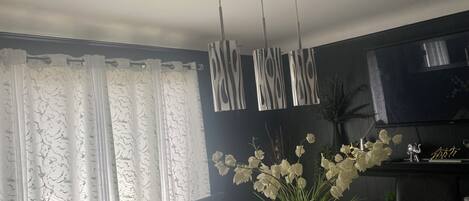 A living room with a TV, a vase with flowers, and a curtain.