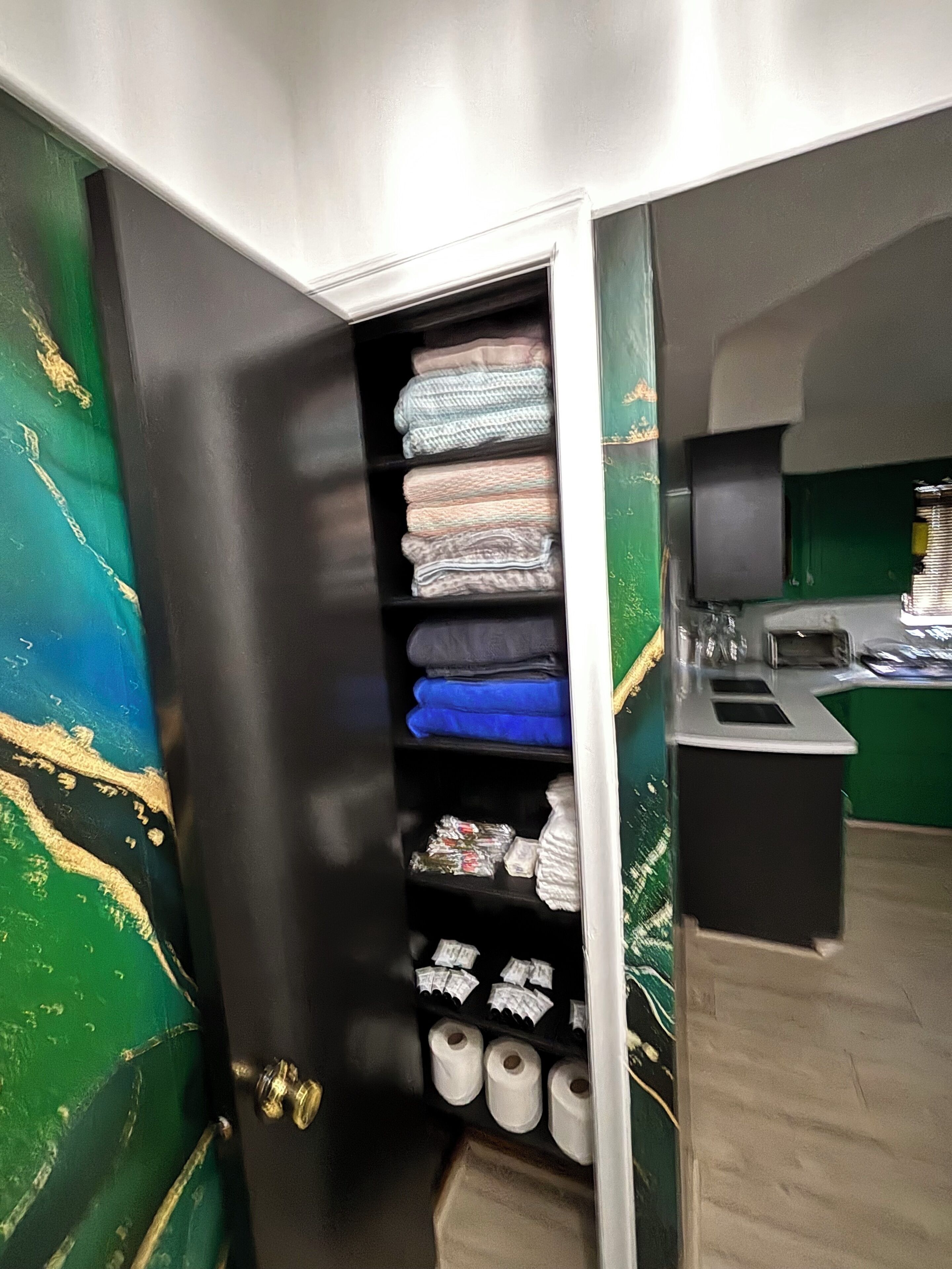 A closet with neatly folded clothes, a shelf with toiletries, and a small desk area with a computer and a cup.