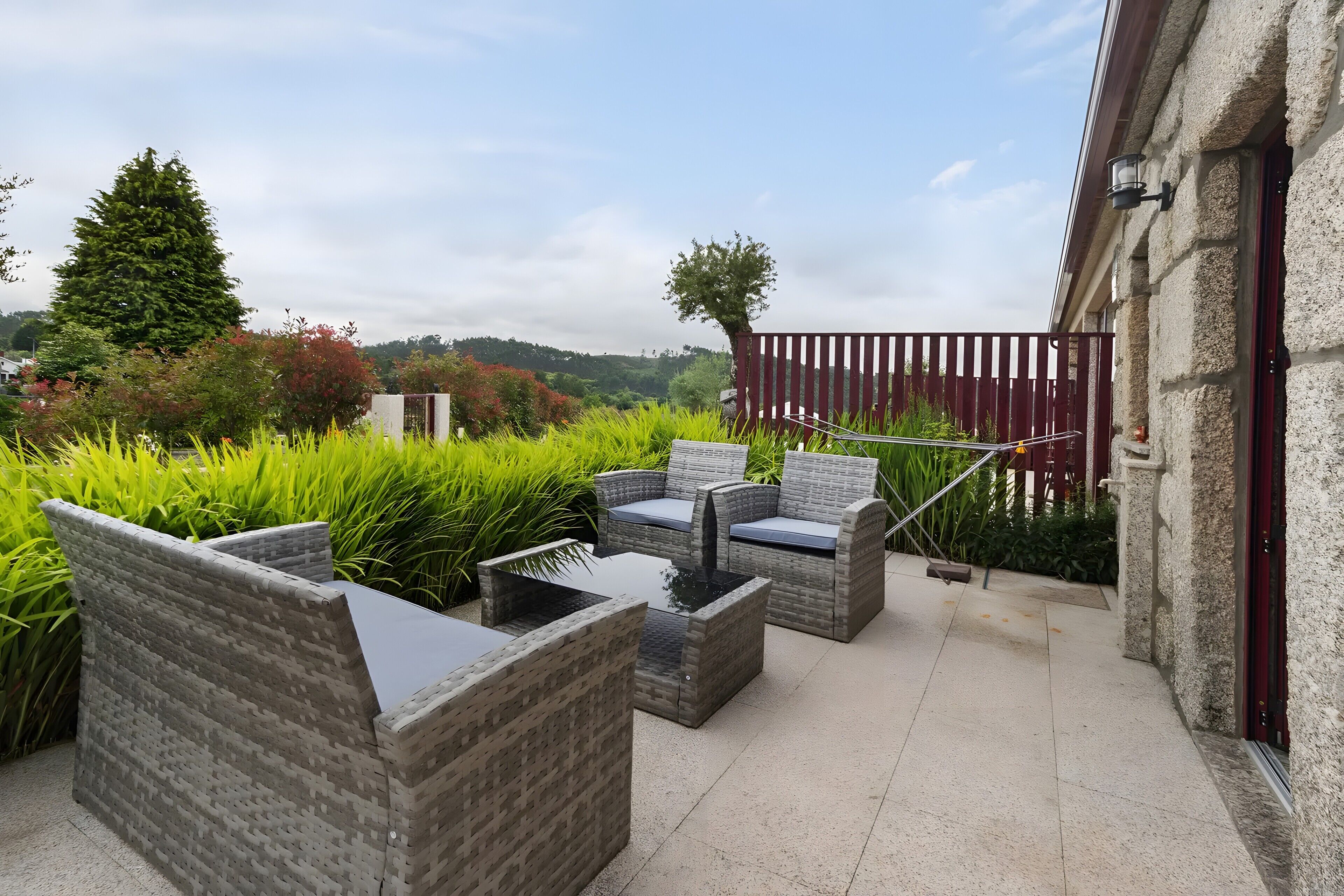 An outdoor patio with wicker furniture, a table, and a view of the surrounding greenery and hills.