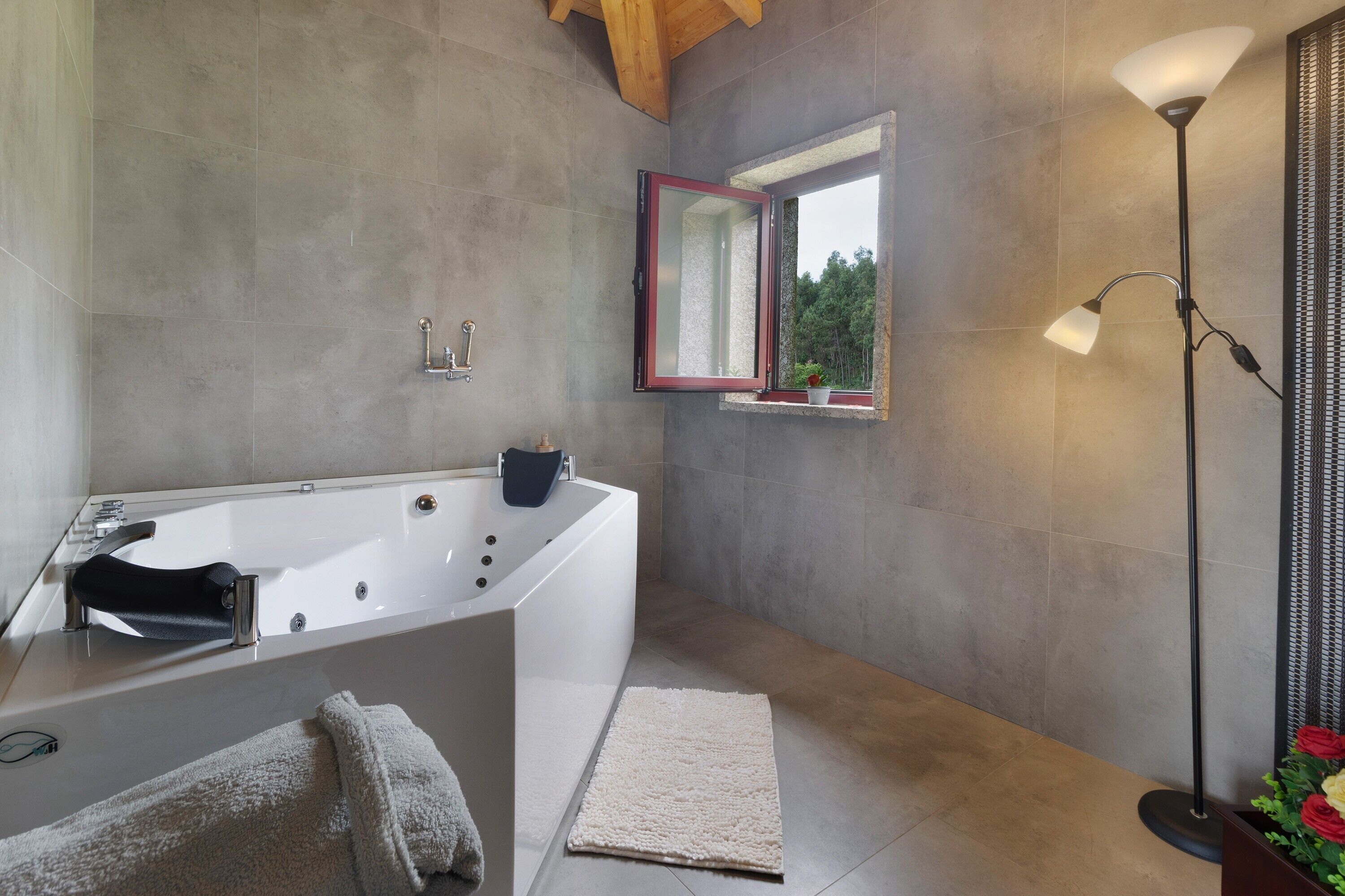 A modern bathroom with a freestanding bathtub, a mirror with a red frame, a floor lamp, and a potted plant.