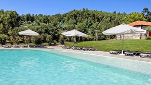 A swimming pool with lounge chairs and umbrellas, surrounded by greenery and a stone building. - Holiday Home 'Lagar T1' with Lake View, Wi-Fi & Air Conditioning (Vieira do Minho)