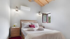 A bedroom with a wooden ceiling, a bed with white bedding, a red pillow, a nightstand with a lamp, and a window with a view. - Holiday Home 'Lagar T1' with Lake View, Wi-Fi & Air Conditioning (Vieira do Minho)