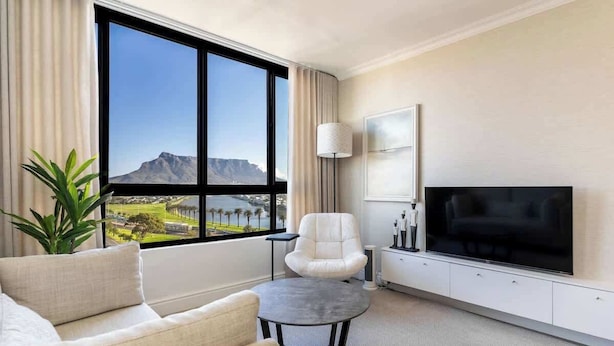 Een moderne hotelkamer met een groot raam en uitzicht op de bergen, een flatscreen televisie, een bank, een stoel en een klein tafeltje.