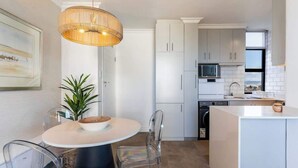 Een moderne keuken met witte kasten, een ronde eettafel met stoelen en een hangende lamp.