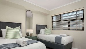 A hotel room with two beds, a large mirror, a nightstand, and a window with blinds.