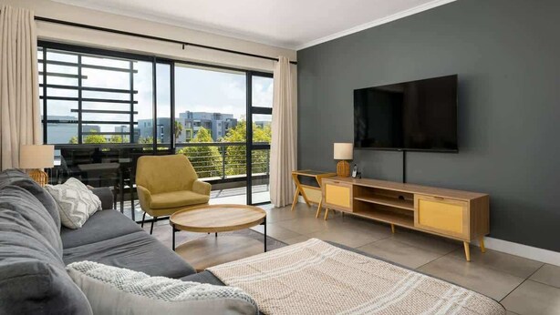 A modern living room with a sofa, armchair, round table, and TV.