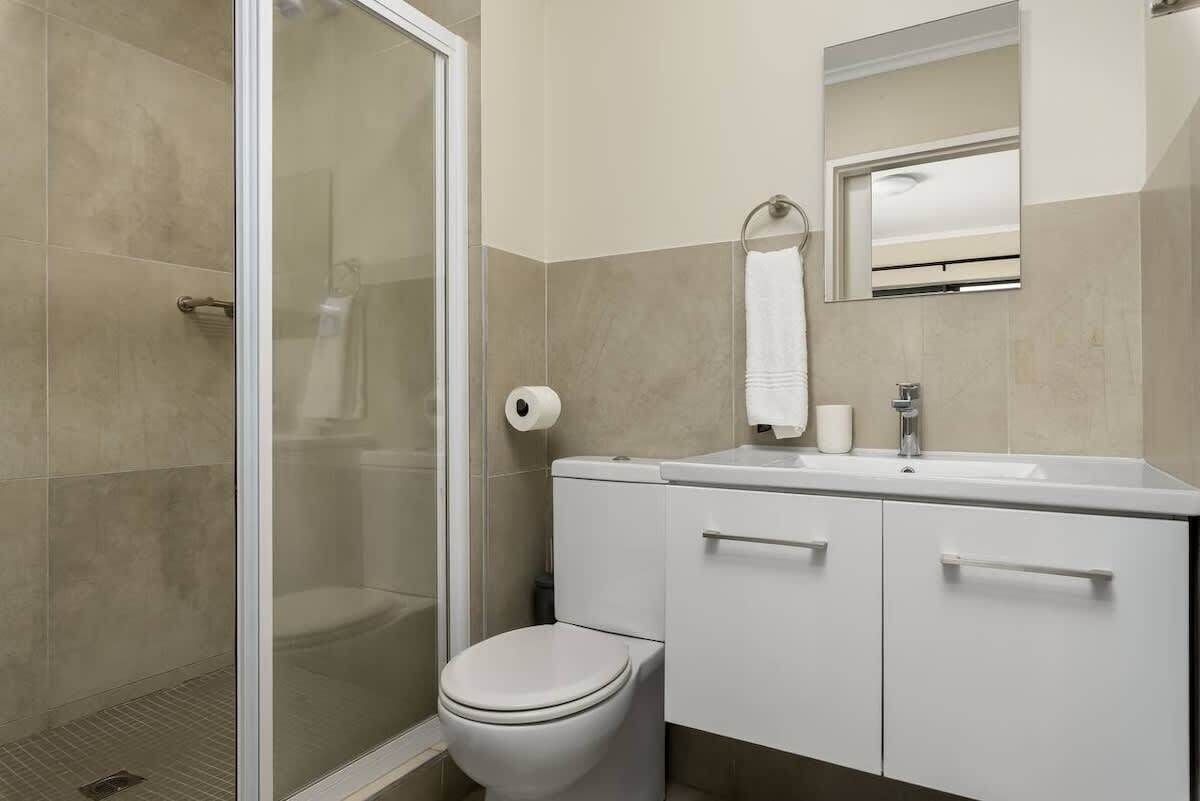 A modern bathroom with a glass shower enclosure, a toilet, a sink with a mirror, and a towel rack.