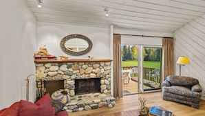A cozy living room with a stone fireplace, a comfortable sofa, and a view of the outdoors. - Fairway Haven with Private hot tub! Dog Friendly! (Sun Valley)