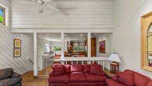 A spacious living area with a red sofa, patterned armchair, and wooden coffee table. A kitchen is visible in the background. - Fairway Haven with Private hot tub! Dog Friendly! (Sun Valley)