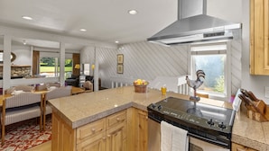 A kitchen with a central island, wooden cabinets, a stainless steel range hood, and a view of the outdoors. - Fairway Haven with Private hot tub! Dog Friendly! (Sun Valley)