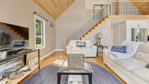 A spacious living room with a high ceiling, a staircase, a television, and a sofa with a decorative pillow.