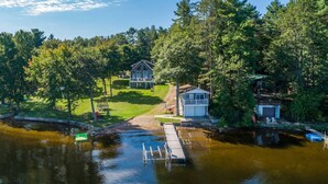 A lakeside property with a dock, a small white building, and a larger house with a porch.