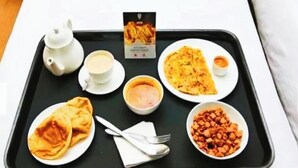 A tray with a teapot, cups, a plate of flatbread, a bowl of chickpeas, a plate with a folded flatbread, and a small bowl of sauce. - Aaron Residency  (New Delhi)